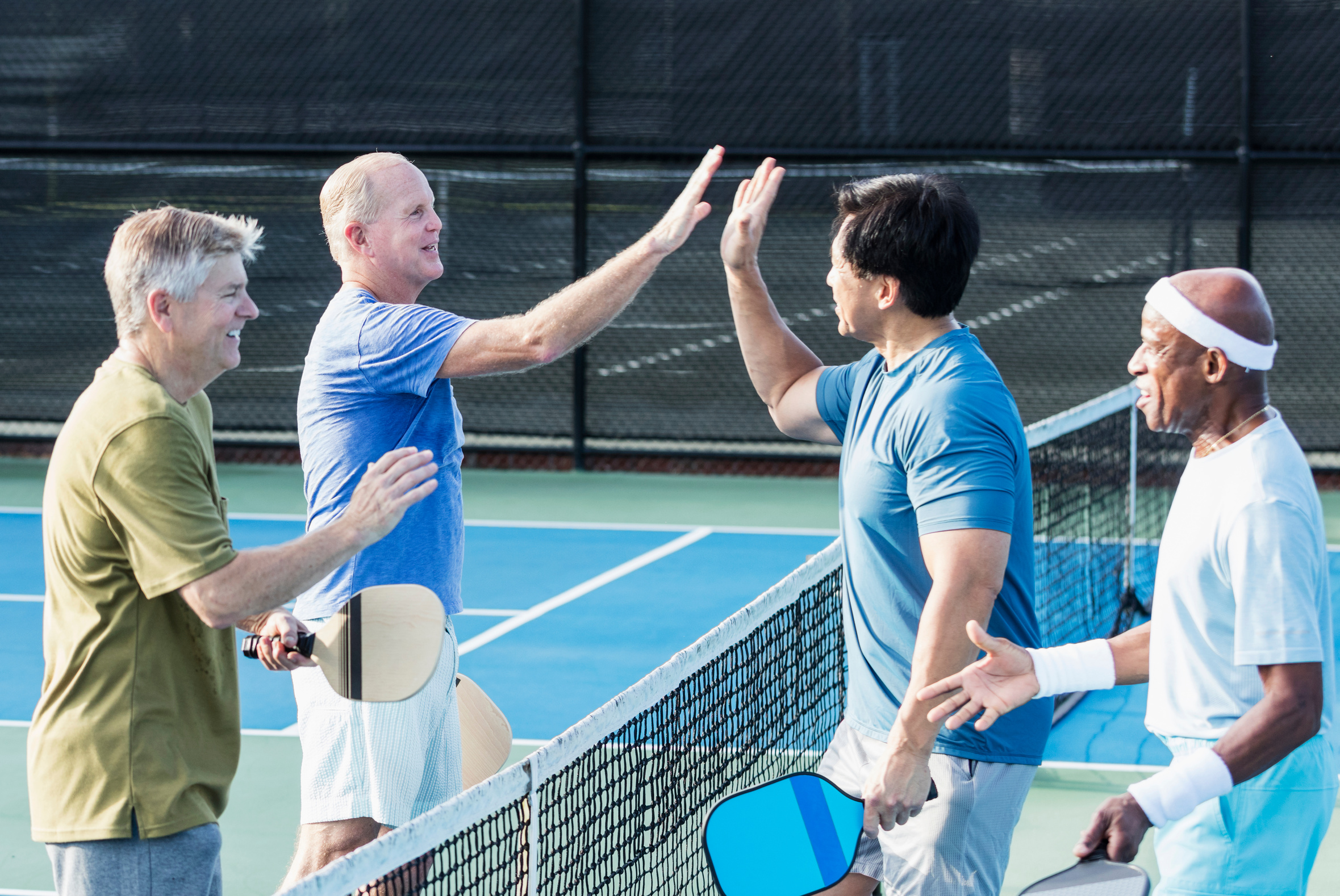 Group of senior men on pickleball court, high-five